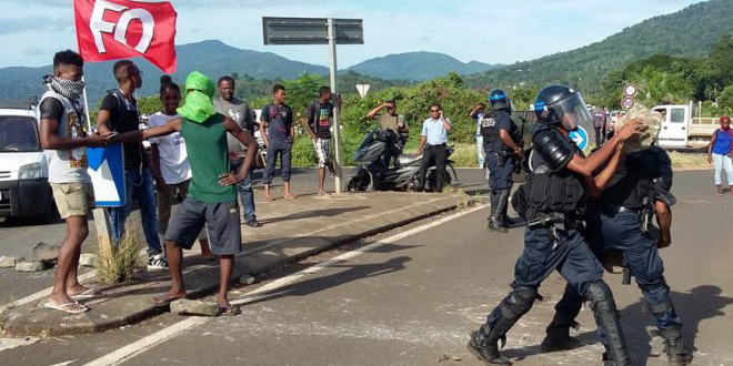 © MAYOTTE 1ÈRE Des gendarmes mobiles dégagent les obstacles sur un barrage routier, sous l'oeil de jeunes manifestants cagoulés.