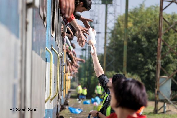 Des bénévoles distribuent des vivres aux réfugiés. Une fois les portes fermées, ils n’ont plus le droit de descendre du train. Zakany (Hongrie), octobre 2015. © Saer Saïd